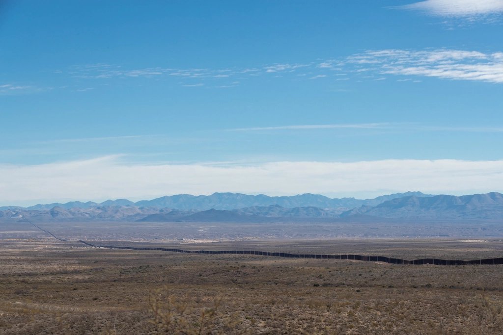 Border barrier stretching across open desert toward distant mountains