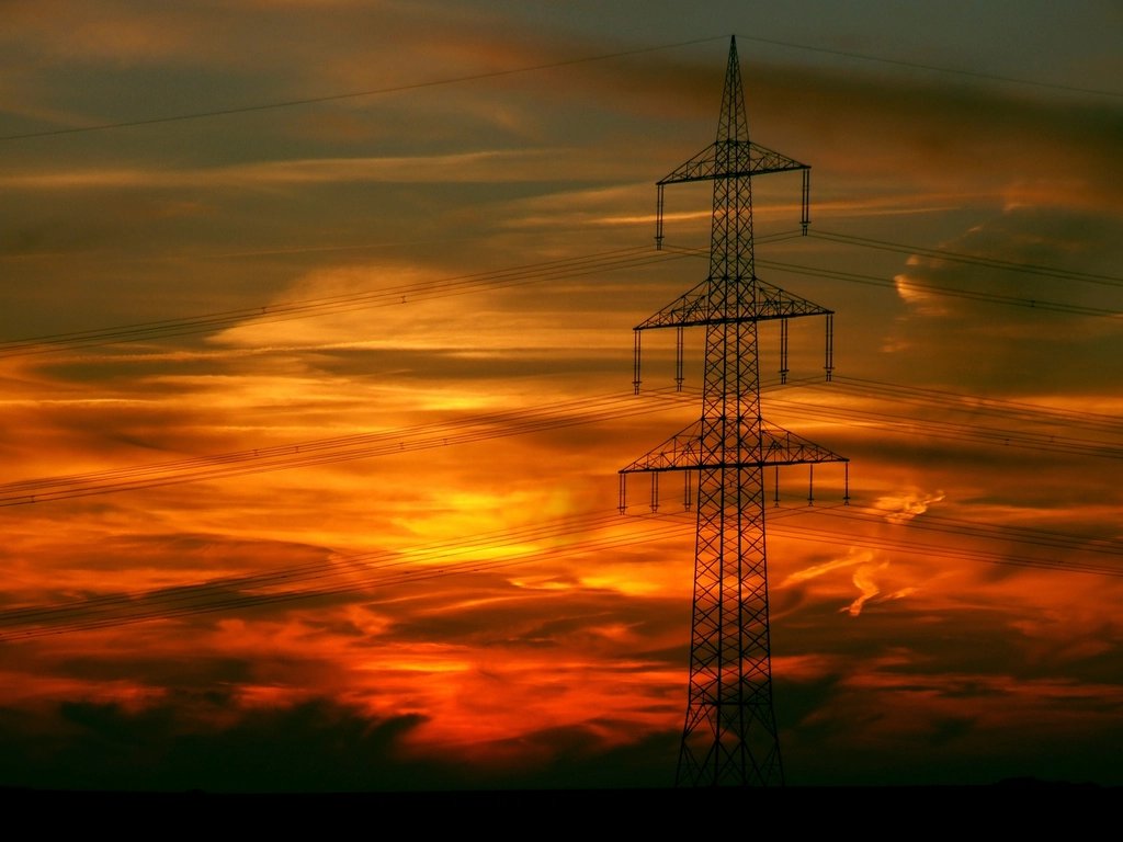 Transmission tower silhouetted against a burning sunset sky