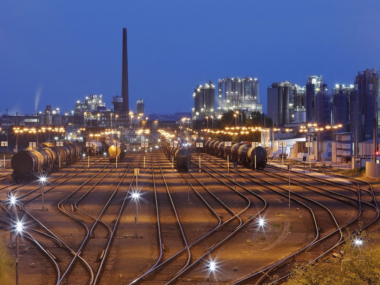 Rail yard at dusk with tank cars fanning toward an industrial skyline